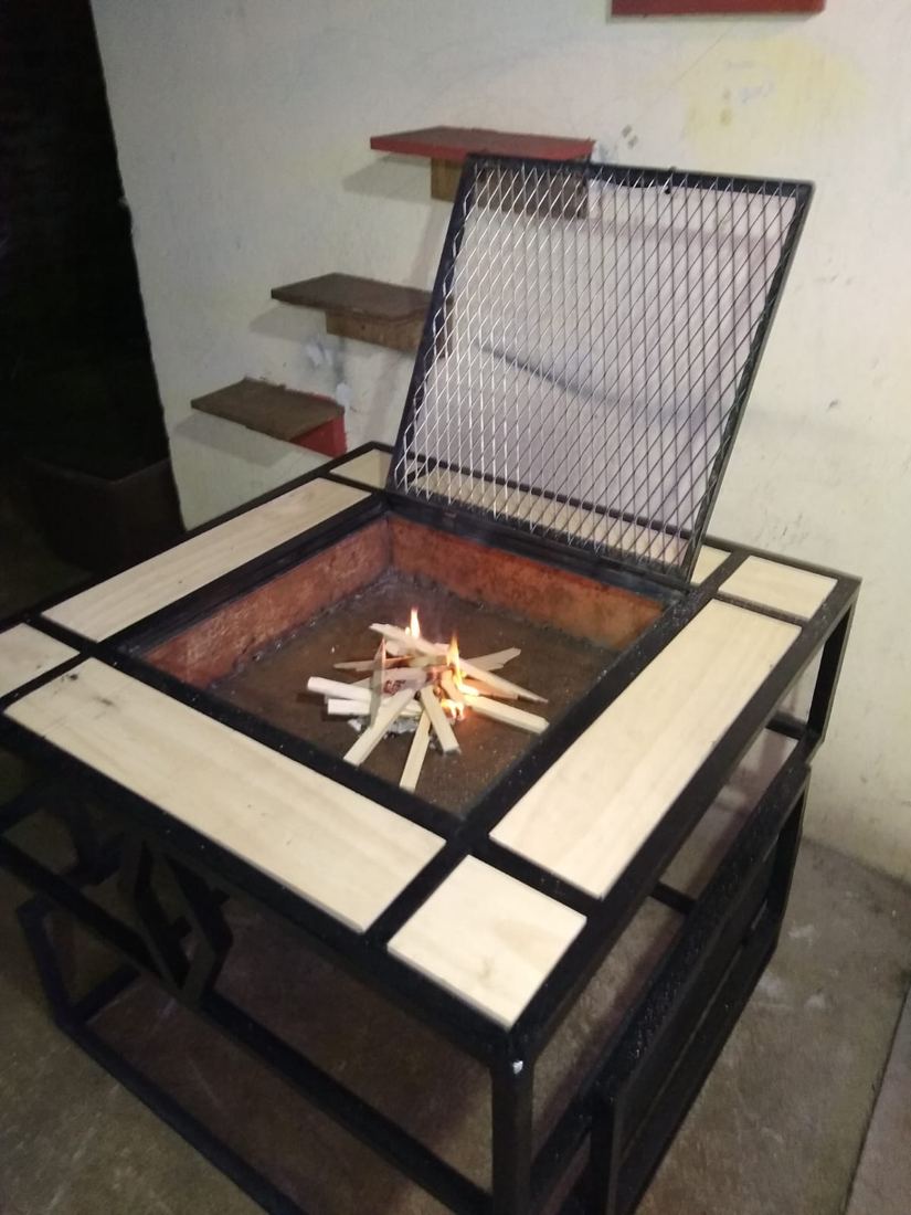 Mesa fogón con tapa de malla abierta y fuego encendido